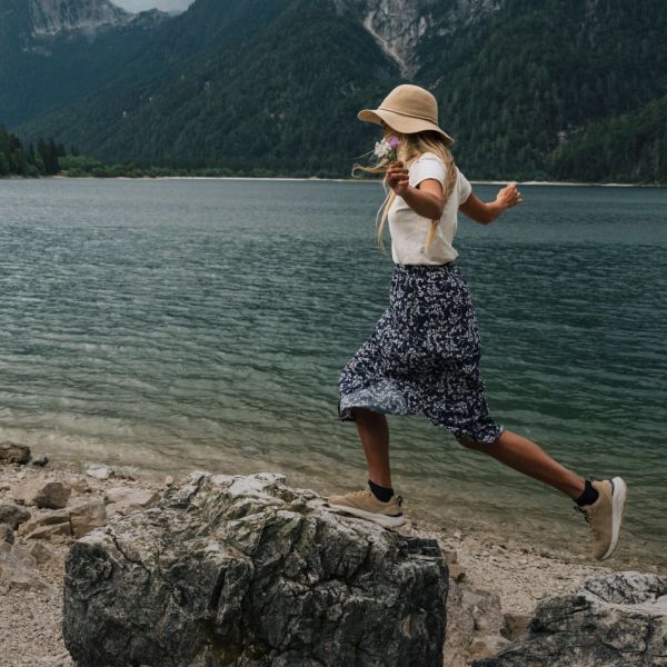 Vrouw in zomerse outdoor-kleding balanceert op stenen bij een meer
