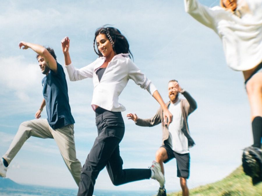 Vier mensen in zomerse wandelkleding rennen over een veld