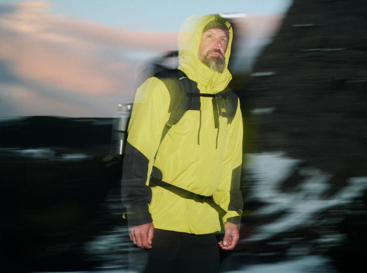Man in fel geel jack en met rugzak tijdens het wandelen in de avondschemering, bewegingsonscherpte geeft de foto dynamiek.