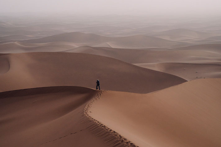 Een man staat op een duin in de zandwoestijn