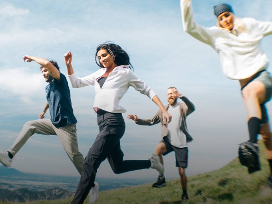 Vier mensen in zomerse wandelkleding rennen over een veld