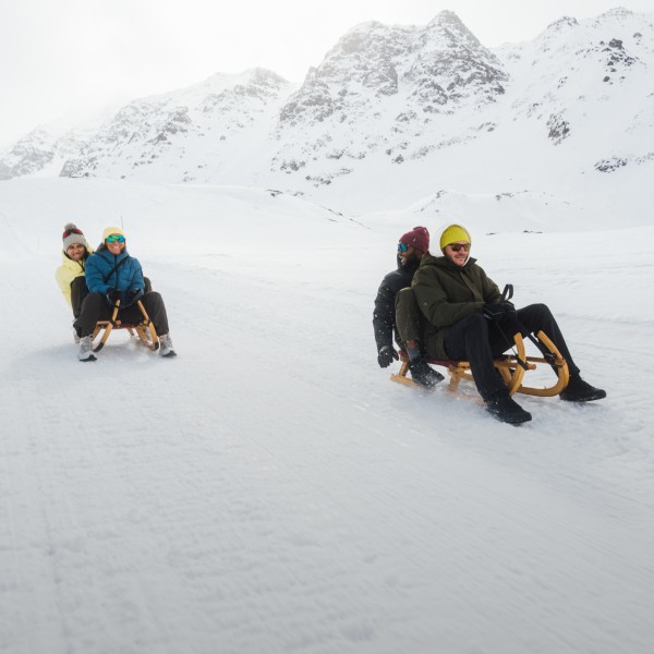 Drie personen zitten op een slee in de&nbsp;sneeuw.