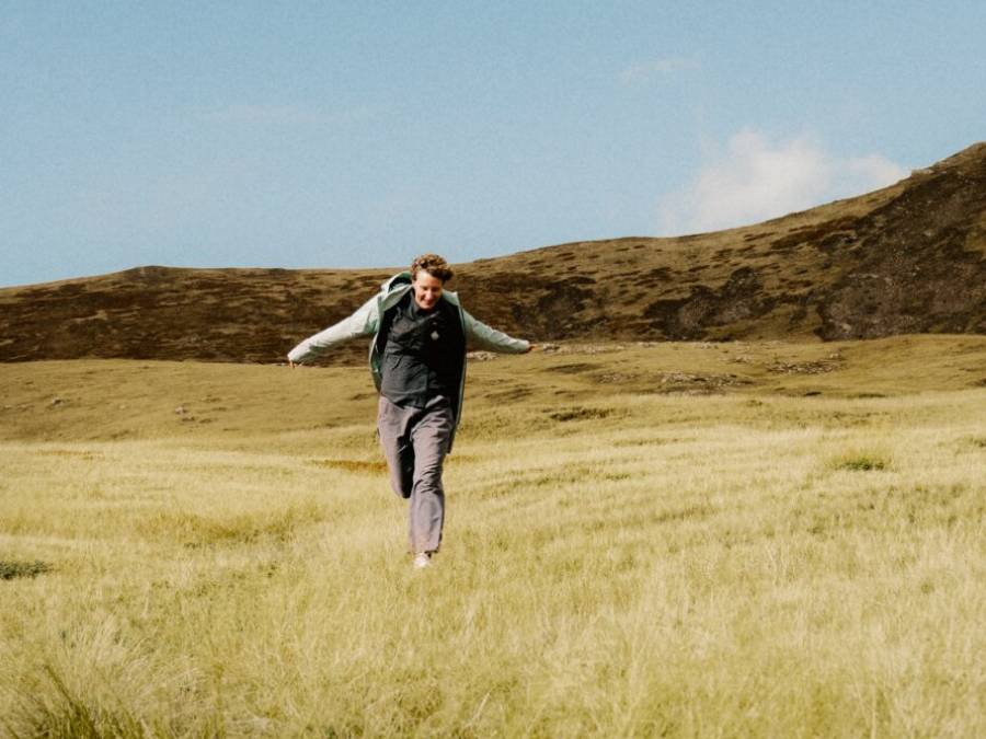Man in zomerse wandelkleding rennend over een veld met uitgestrekte armen