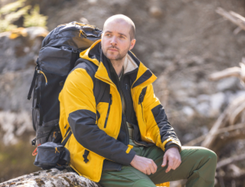 Chris zit met wandelrugzak op een boomstam