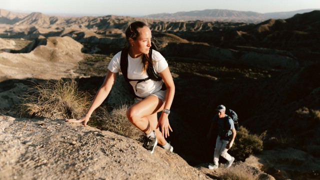 Een vrouw en een man in zomerse wandelkleding klauteren een rots op