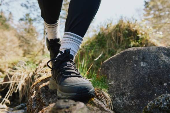 Close-up van een persoon met wandelschoenen aan die over een rotssteen loopt